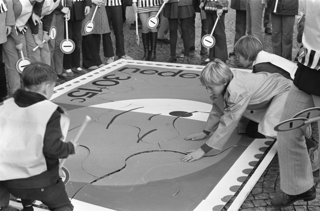 Schwarz-weißes Foto von Kindern, die Hopse spielen, einige halten Stöcke in den Händen.