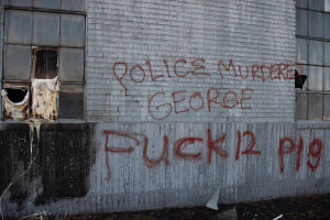 Ein Gebäude mit Graffiti, das "Polizei Mord George Fuck 12 P19" lautet, mit Fenstern und diversen Gegenständen vor dem Gebäude.