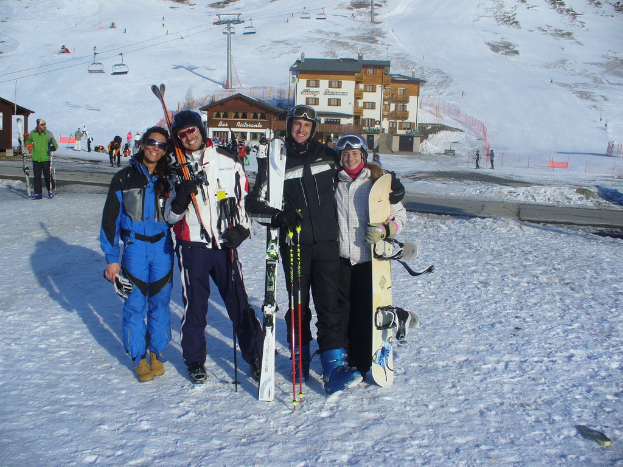 Vier Personen posieren für ein Foto mit Schlittschuhschützern und Werkzeugen vor einem schneebedeckten Berg im Hintergrund.