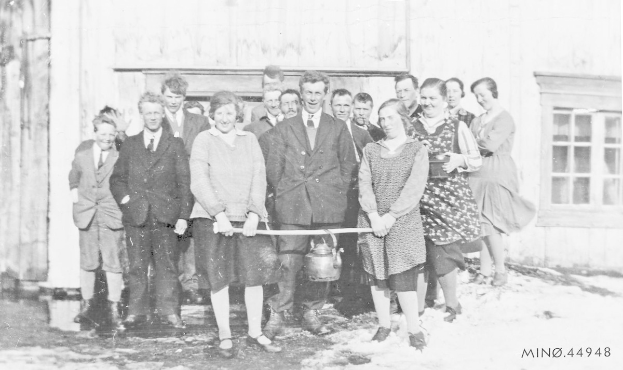 Schwarzes und weißes Foto von Menschen, die lächeln und ein Band vor einem Gebäude mit einem Fenster und einer Tür halten, bei der Einweihung einer neuen Schule.