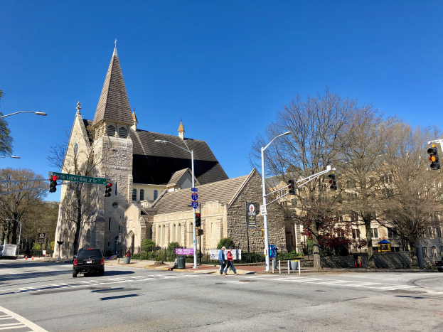 Die Episkopalkirche St. Lukas, eine große Kirche mit einem Turm, steht an einer Straßenkreuzung umgeben von Gebäuden, Fahrzeugen, Fußgängern und Bäumen unter einem klaren blauen Himmel.