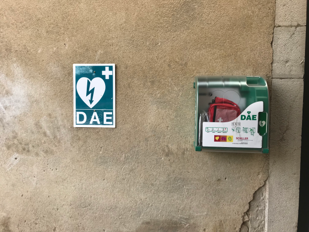 Eine Wand mit einem Schild, auf dem "Dae" steht und einer Box mit einem Defibrillator-Beutel.