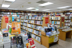 Ein gut organisierter Buchladen mit ordentlich aufgestellten Büchern auf Regalen und Tischen, mit informativen Schildern auf dem Boden und Deckenleuchten.