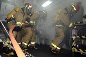 Feuerwehrleute in Schutzausrüstung arbeiten an einem Löschfahrzeug mit Ausrüstungsgestellen und Hintergrundinfrastruktur.