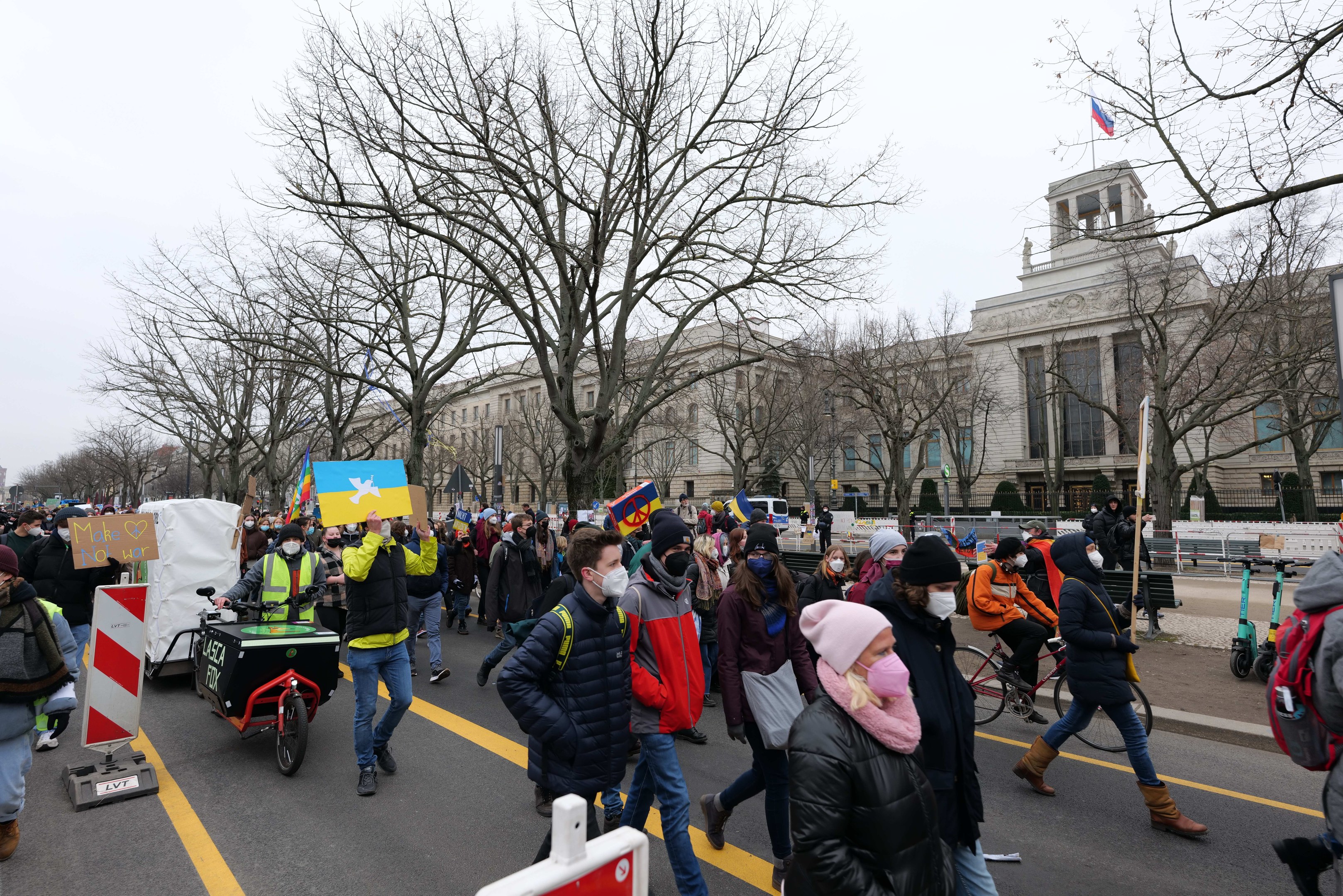 Eine große Gruppe von Menschen nimmt an einer Protestmarsch in Washington, D.C. am 21.01.2020 teil, geht eine Straße entlang und hölt Plakate und Banner, einige fahren Fahrráder, mit Bäumen und Schildern im Hintergrund bei einem klaren blauen Himmel.