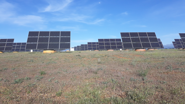 Ein Feld voller Solarpanels auf einer grünen Wiese mit Hügeln und Wolken im Hintergrund.