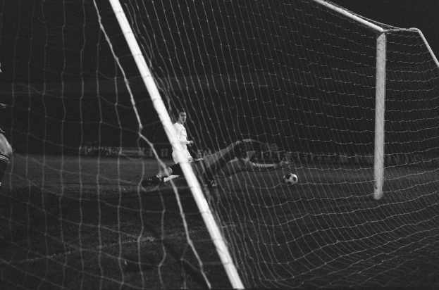 Ein Fußballer in Schwarz und Weiß, der einen Ball in der Luft abwehrt, vor einem Netz im Hintergrund.