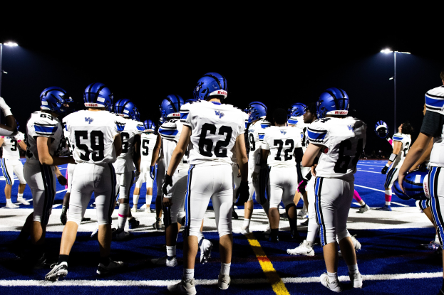 Eine Gruppe von F%C3%BC%C3%9Fballspielern in Helmen und Stiefeln, die auf einem Feld unter Flutlicht stehen und bereit zum Spiel zu beginnen scheinen.