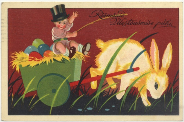 Alte Postkarte mit einem Baby in einem Zylinder, das einen Karren voller bunter Ostereier schiebt, neben einem Hasen, mit handgeschriebenen Ostergrüßen.