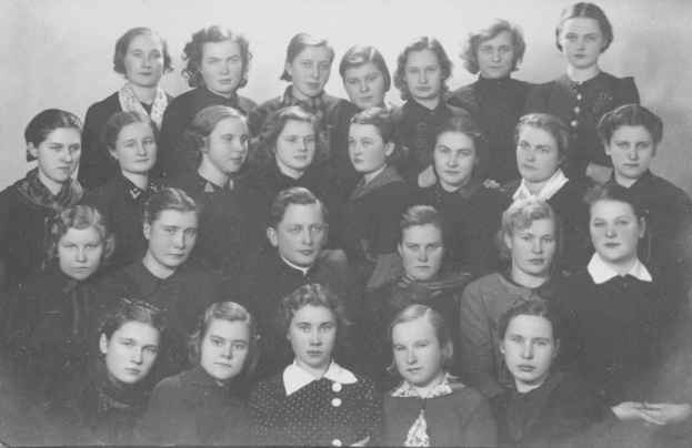 Ein Schwarz-Weiß-Foto einer Gruppe von Frauen in Schuluniformen mit einer Wand im Hintergrund und Text unten mit der Aufschrift "1918-1918 Schulmädchen".