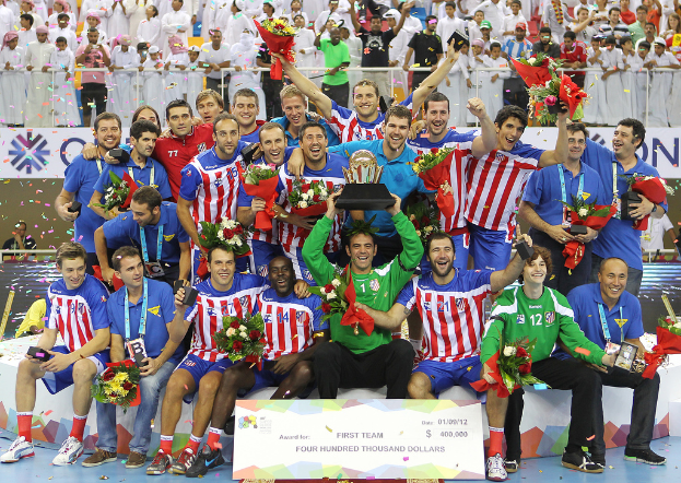 Eine Gruppe von Menschen in Sportbekleidung, einige halten einen Award und Blumen, stehen vor einer Menge mit Geländern und Tafeln im Hintergrund.
