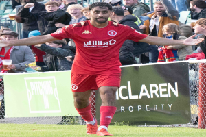 Ein Fußballspieler in roter Uniform rennt mit ausgestreckten Armen auf einem Feld, umgeben von Zuschauern hinter einem Zaun, mit einem Banner "Middlesbrough FC v Swansea City - Sky Bet Championship" im Hintergrund.