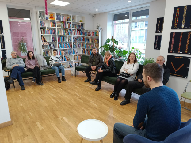 Eine Gruppe von Menschen sitzt um einen Tisch in einem Raum mit Bücherregalen, Pflanzen und einem Fenster, die sich während einer Workshop-Veranstaltung über die Zukunft von Gesundheit und Wohlbefinden in Berlin unterhalten.