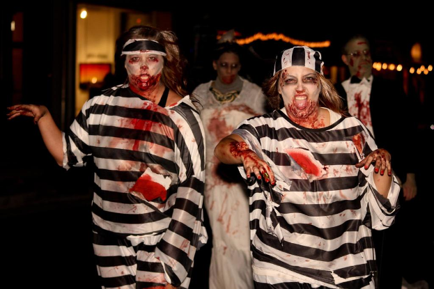 Zwei Frauen in Schwarz-Wei├čer Kleidung mit Zombie-Make-up stehen im Vordergrund, dahinter ein Paar in anderer Schminke und Lichter im Hintergrund.