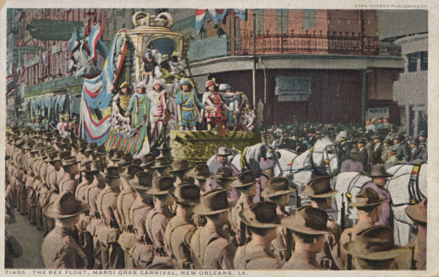 Eine alte Postkarte zeigt einen Mardi Gras-Umzug in New Orleans, mit einem Float, der mit Flaggen und Gegenständen geschmückt ist, Menschen auf Pferden und Zuschauern am Straßenrand, mit Gebäuden im Hintergrund und der Aufschrift "The Rex Float, Mardi Gras Carnival, New Orleans" unten.