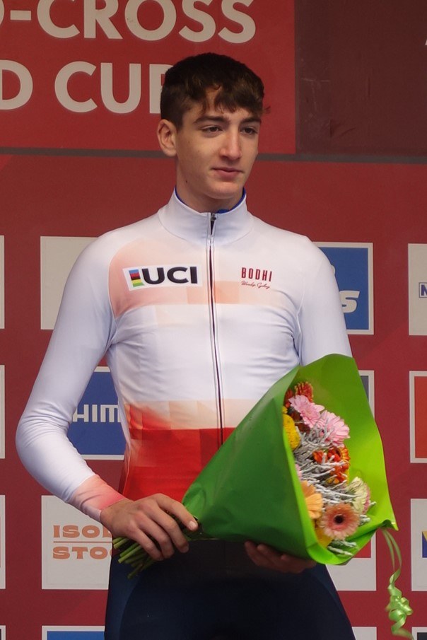 Ein Mann steht auf einem Podium und hält einen Blumenstrauß, feierlich mit einem selbstbewussten und stolzen Gesichtsausdruck.