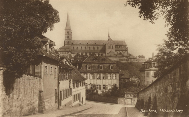 Schwarz-weiß-Foto einer Stadtstra├če in Bamberg, Deutschland, mit einer Kirche im Hintergrund, flankiert von W├Ąnden und gesäumt von B├Ąumen.