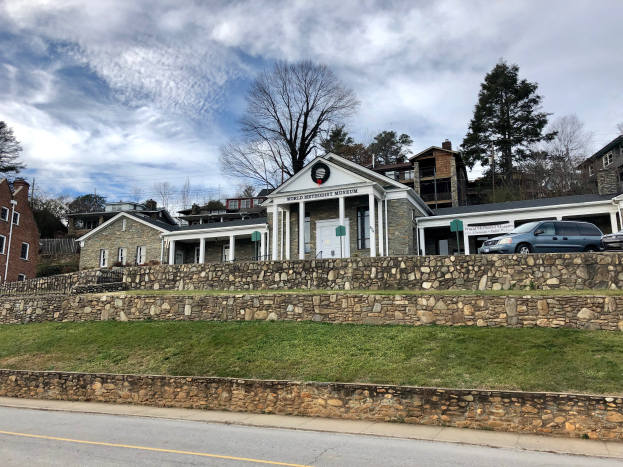 Steinwand mit geparkten Autos davor, flankiert von Gebäuden mit Fenstern, Türen und Bäumen, unter einem bewölkten Himmel; das Welterbe-Museum, kürzlich wiedereröffnet.