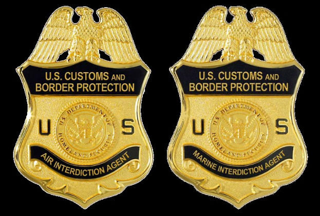 Zwei goldfarbene Abzeichen mit 'U.S. Customs and Border Protection'-Text auf einem weißen Hintergrund.