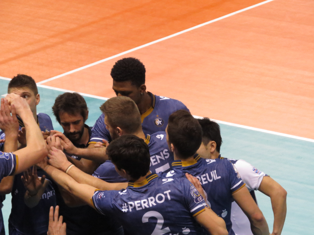 Eine Gruppe von Männern in blauen 'Ligue 1'-T-Shirts feiert auf einem Volleyballfeld, einige mit erhobenen Händen.