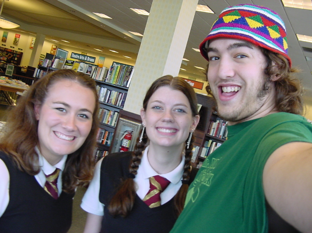 Ein Mann und zwei Studenten machen ein Selfie in einer Bibliothek, mit Regalen voller B├╝cher im Hintergrund.