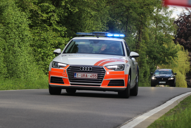Ein Audi A4-Polizeifahrzeug fährt auf einer Straße neben einem Wald, mit zwei Insassen, Gras auf beiden Seiten und einem klaren blauen Himmel im Hintergrund.