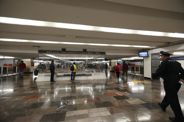 Ein voller U-Bahnhof mit Menschen, einem Polizeibeamten im Vordergrund, Leuchtschildern und -anlagen sowie verstreuten Geländern und Gegenständen.