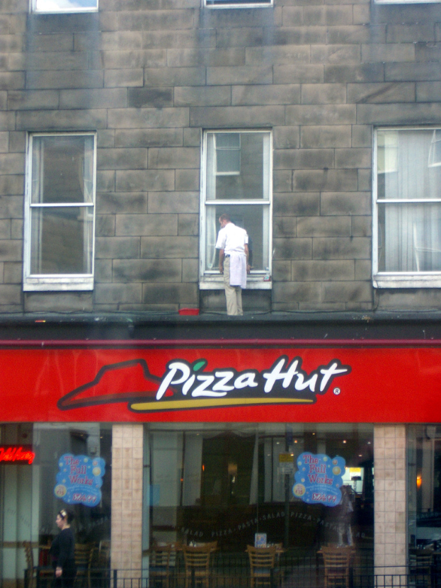 Ein Pizza Hut-Laden mit einem Mann oben, der die Glasscheiben putzt und ein rotes Schild davor.